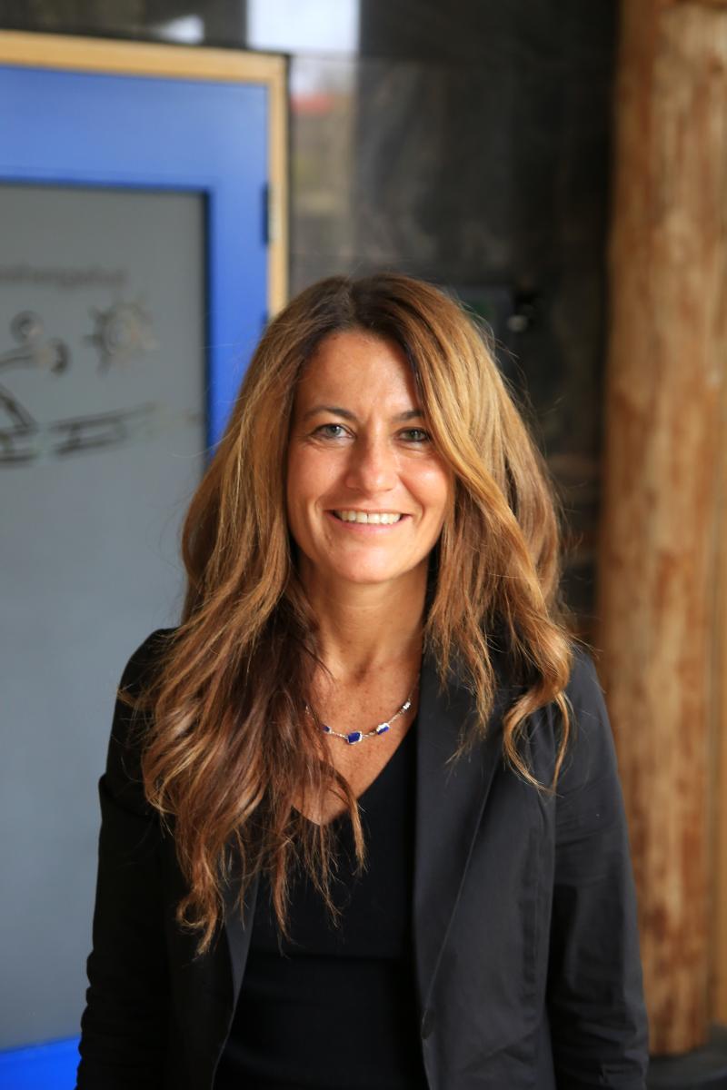 Kvinne, brunt langt hår, ser i kamera, smiler.